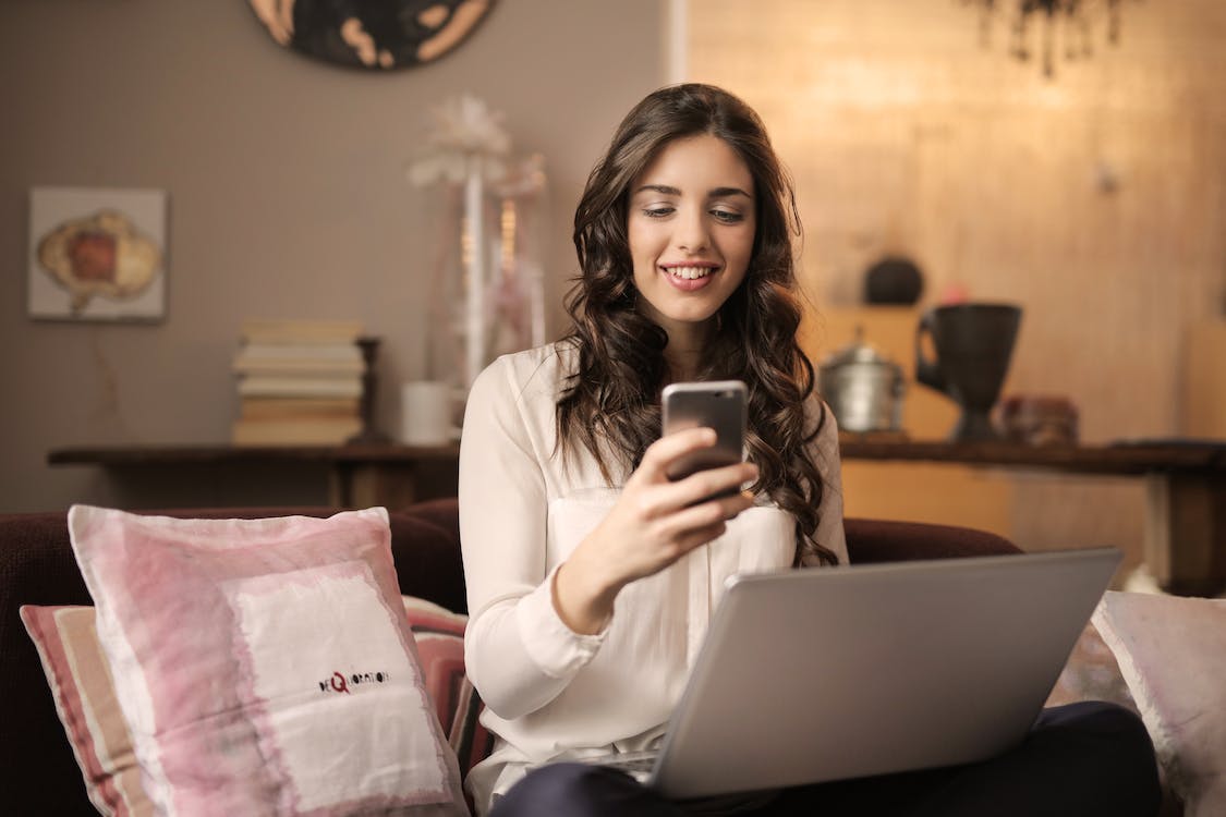 woman with cell phone in hand and laptop computer on lap