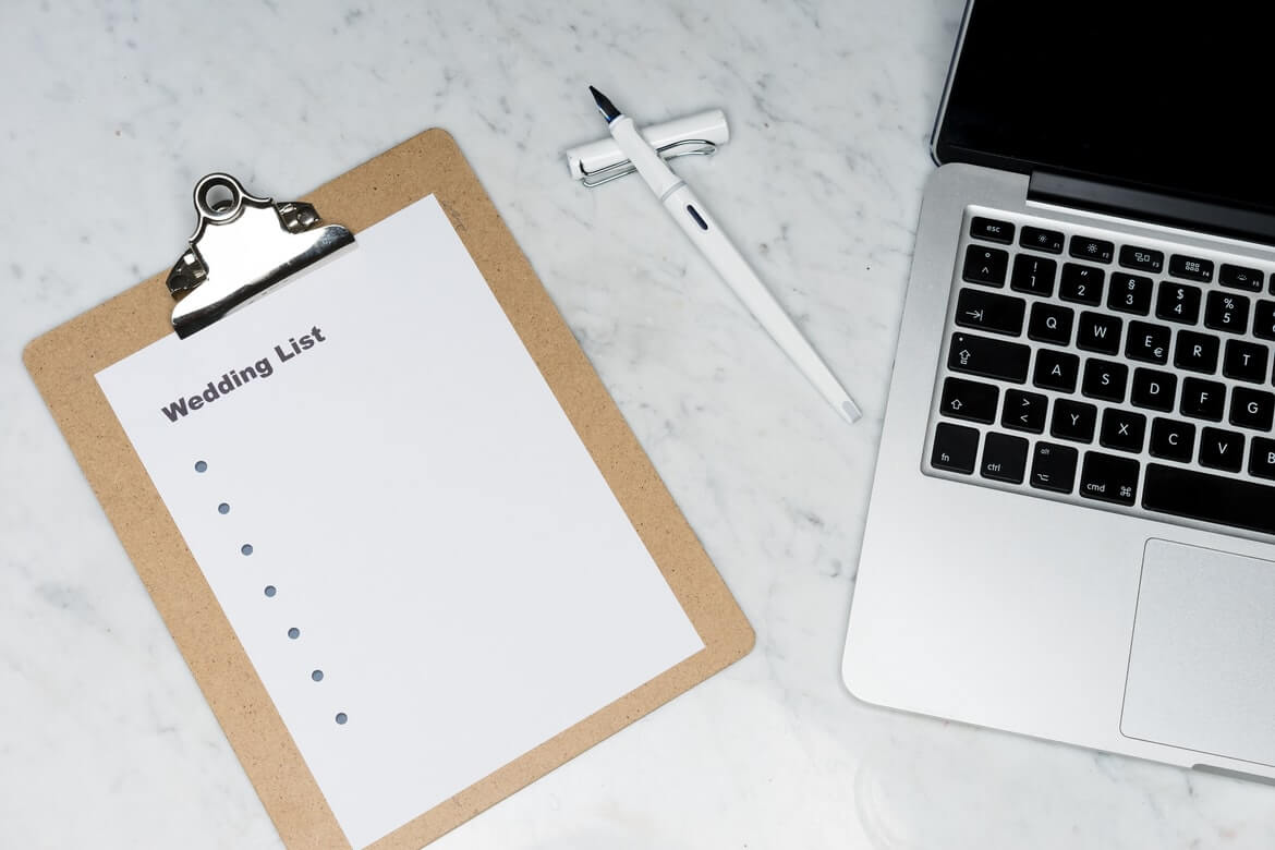 clipboard of wedding list and laptop on table