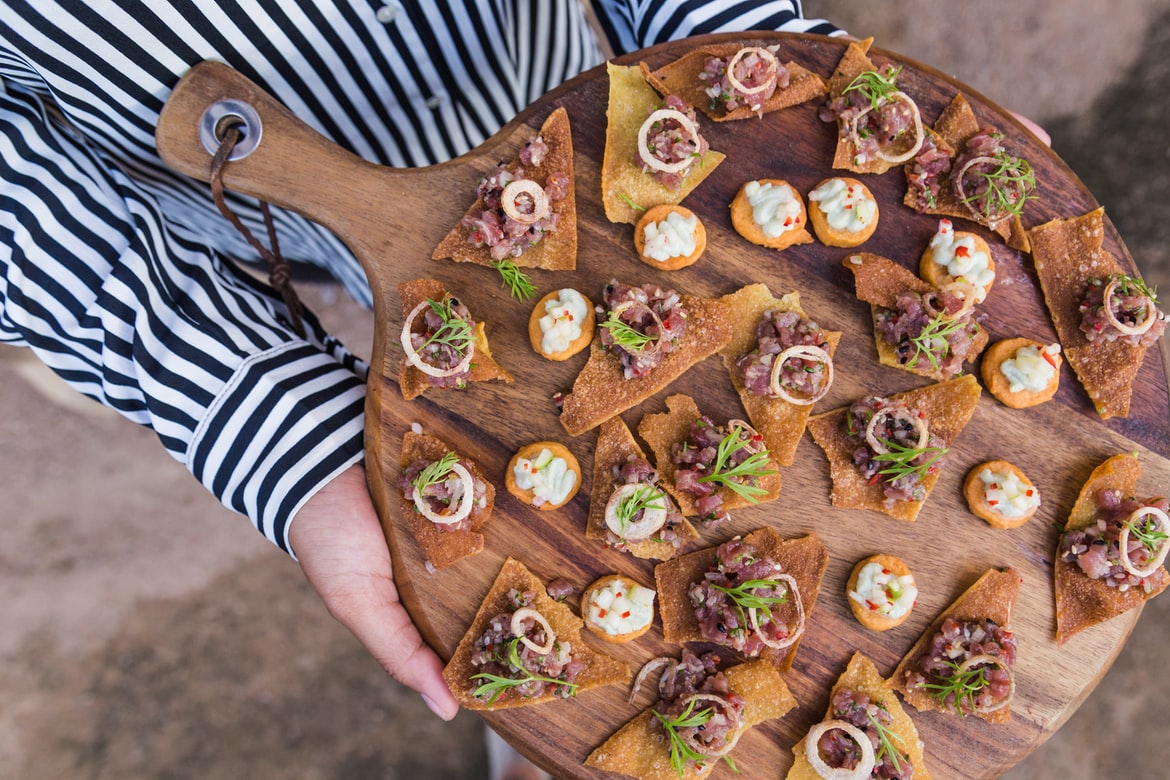 [person holding a cutting board of hors d’oeuvres