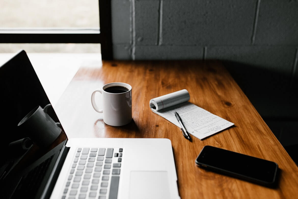 laptop, notepad, cell phone and coffee cup on table