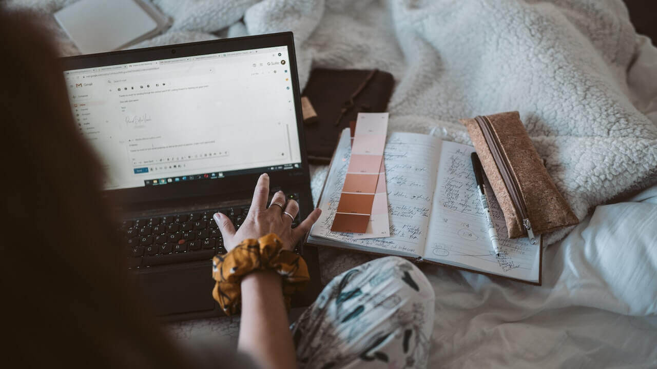 person looking at email on laptop while sitting on bed