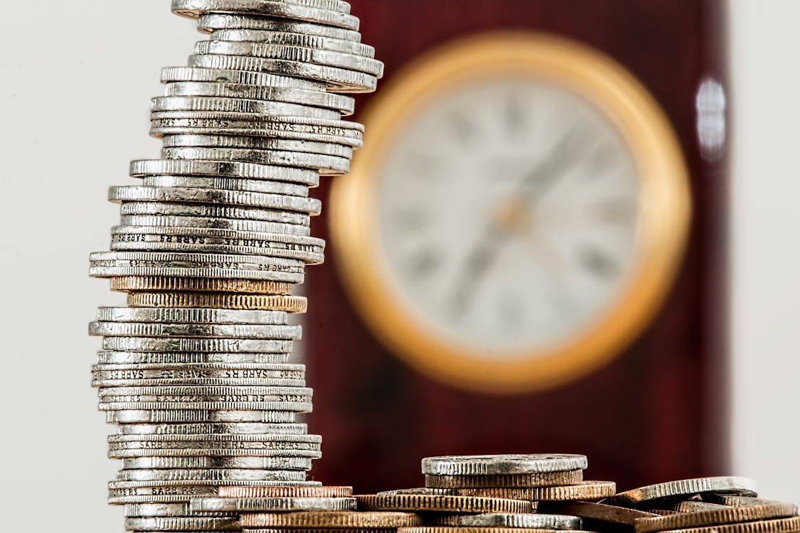 Time money concept image stack of coins in front of out of focus clock