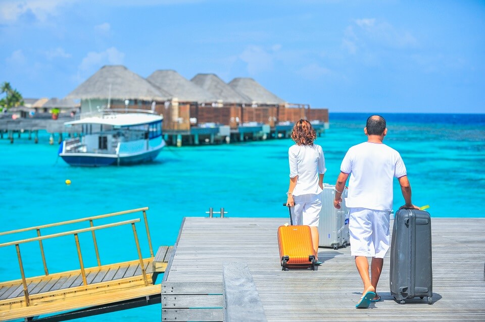 Vacationing couple wheeling luggage to end of pier